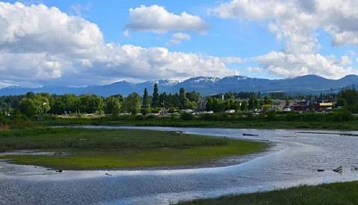 A serene river flows with majestic mountains rising in the background under a clear blue sky.